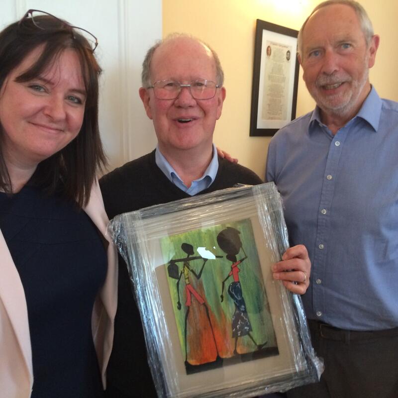 Jenni Barrett, chief executive, and John Cooley, chair of the Board, present a painting from Kenya to Br. Pat Madigan, Community Leader of Edmund Rice House, on the occasion of his retirement.